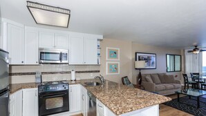 Cocina compacta con microondas, horno y lavavajillas, junto a una sala de estar con sofá y mesa de comedor.