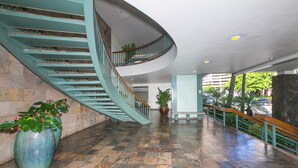 Un vestíbulo espacioso con una escalera curva, plantas en macetas grandes y una pared de piedra.
