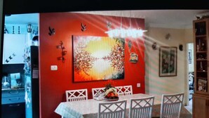 Un coin repas agrémenté d’un mur d’accent rouge, d’un grand tableau abstrait et d’une table dressée pour quatre personnes, avec des chaises blanches.
