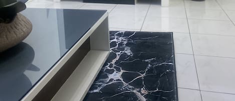 Una sala moderna con un televisor de pantalla plana sobre un soporte blanco, una mesa de centro de mármol, una planta en maceta y flores de orquídea blanca.