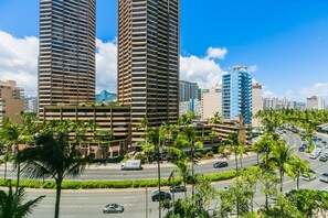 Um edifício alto com design arquitetônico moderno, rodeado por palmeiras e uma rua movimentada com carros.