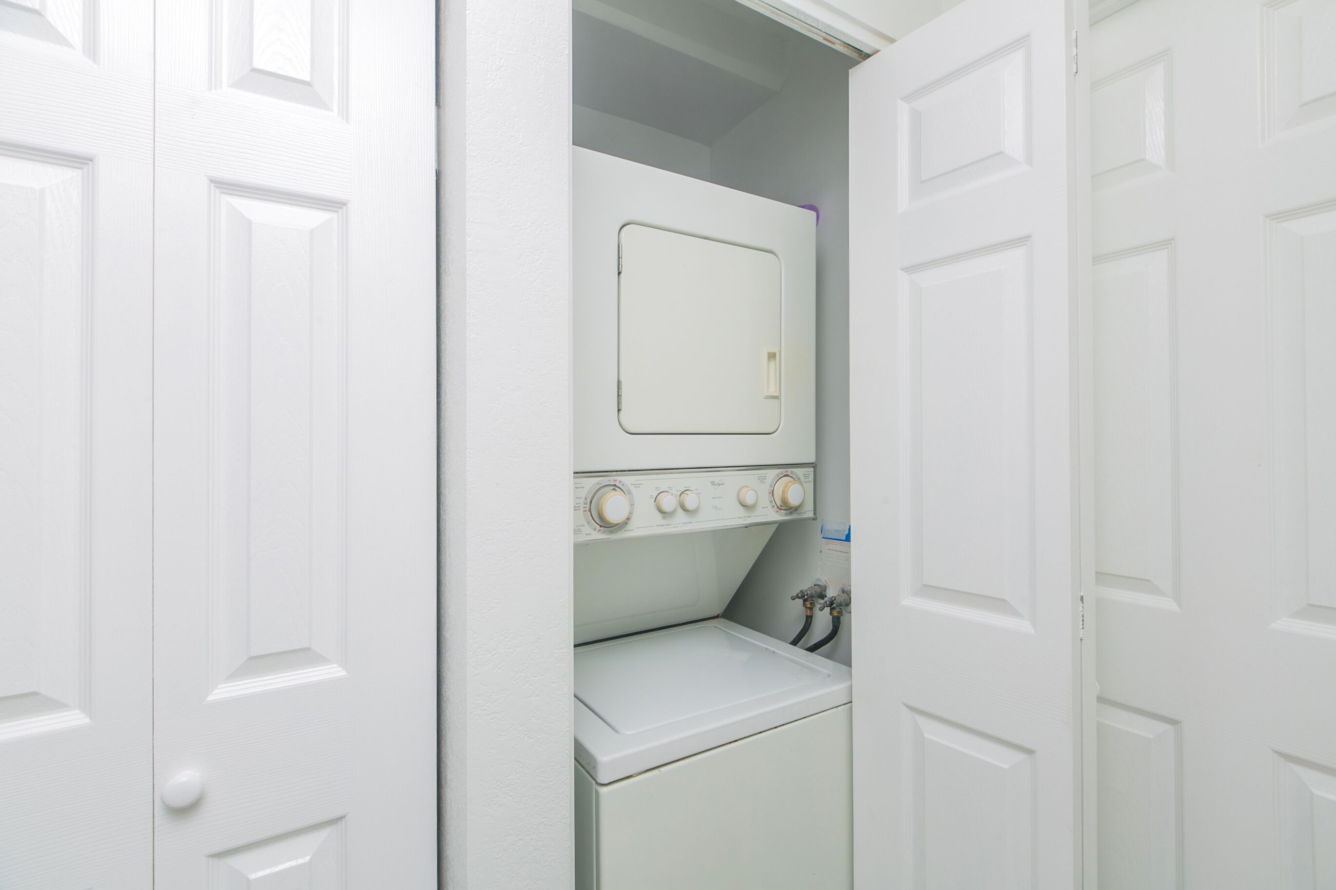 A laundry room with a washing machine and dryer, white doors, and a small window.