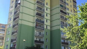 A multi-story residential building with balconies, a parking area with cars, and a clear blue sky.