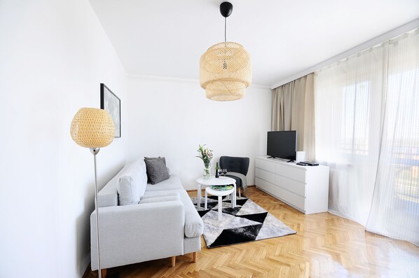 Moderni olohuone, jossa on sohva, sohvapöytä, televisio ja suuri ikkuna, jossa on verhot.