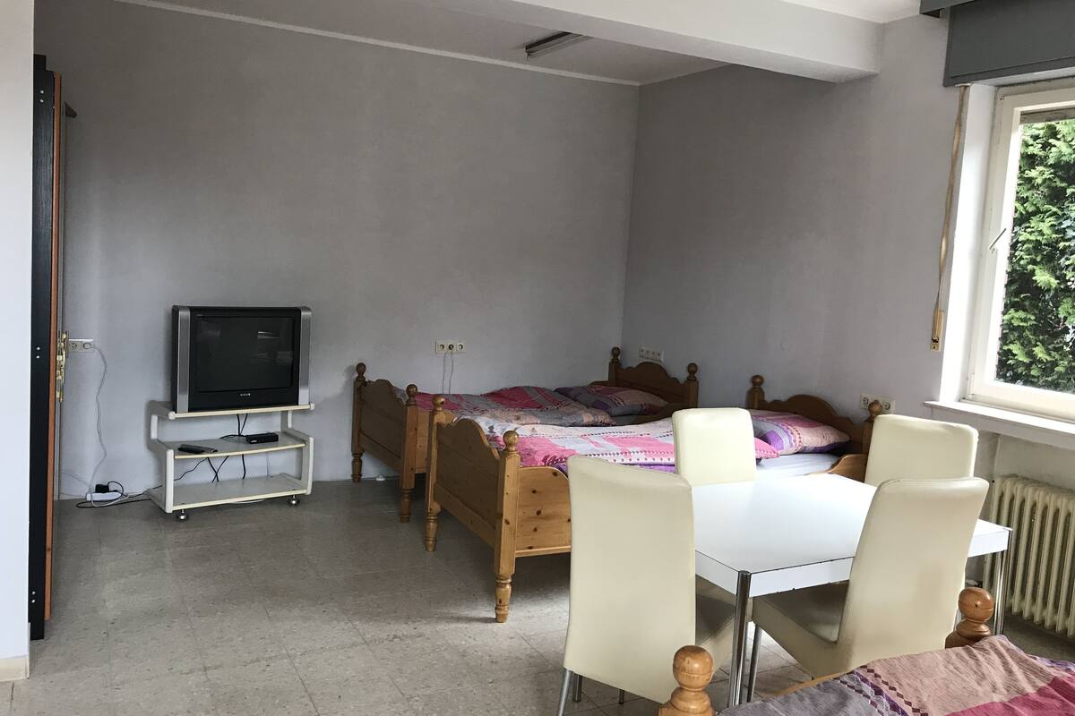 A bedroom with a bed, a TV on a stand, a desk, and a chair.