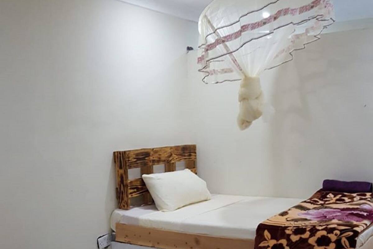 Una habitación pequeña y sencilla con una cama, una mesa de madera y un mosquitero.