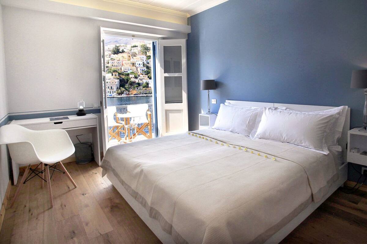 A bedroom with a bed, a desk, a chair, a nightstand, and a view of a balcony with outdoor seating.