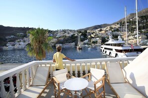 Ein Balkon mit weißen Stühlen und einem Tisch mit Blick auf einen Hafen voller Boote und eine an einem Hügel liegende Stadt.
