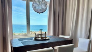 Spiseområde med udsigt til stranden, en lysekrone og et bord med stole.
