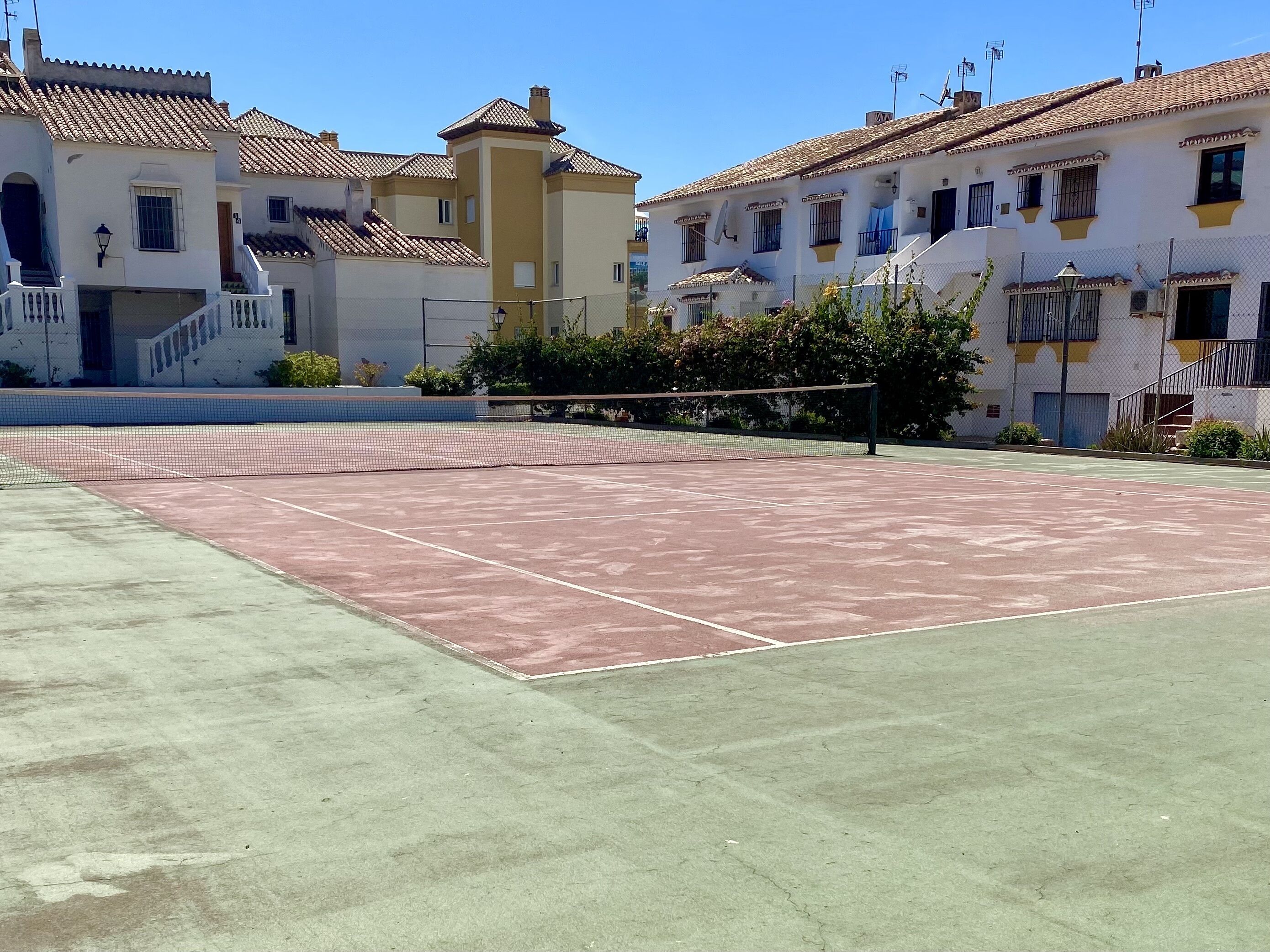 Un campo da tennis circondato da edifici con tetti in tegole e balconi.