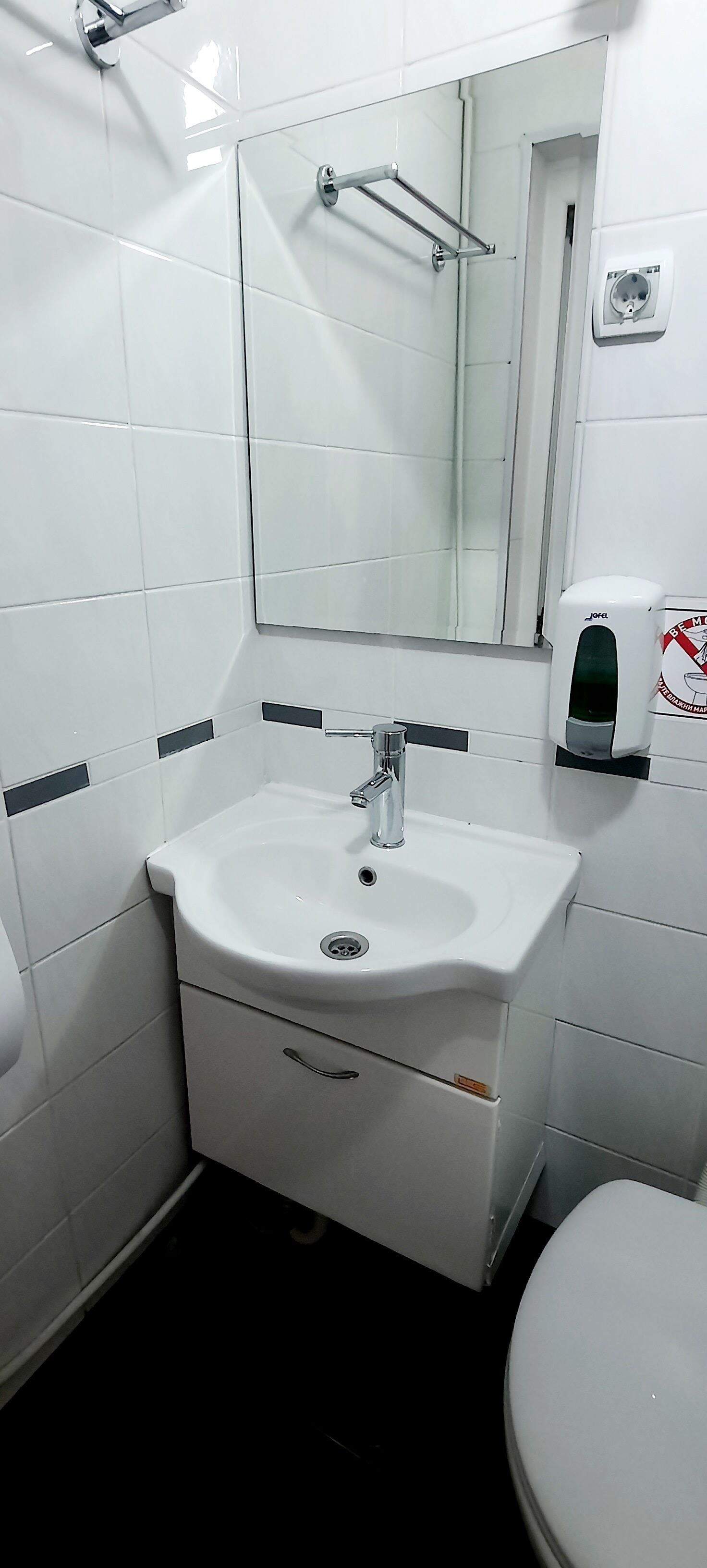Une salle de bain avec un lavabo blanc, un miroir, un sèche-mains et des toilettes.