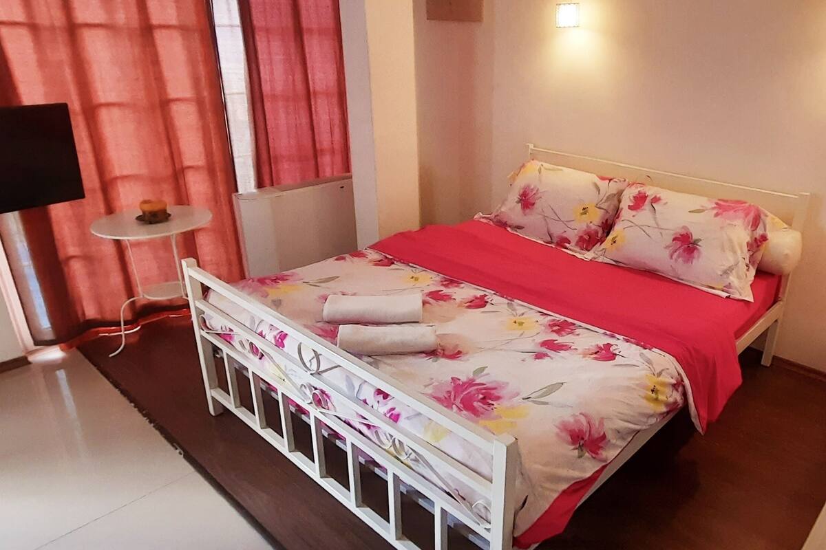Ein Schlafzimmer mit einem Bett, einem Fernseher, einem kleinen Tisch und einer Wandleuchte.