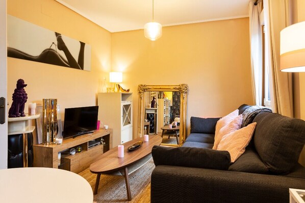 Ein Wohnzimmer mit einer Couch, Fernseher, Couchtisch aus Holz und einem Spiegel.
