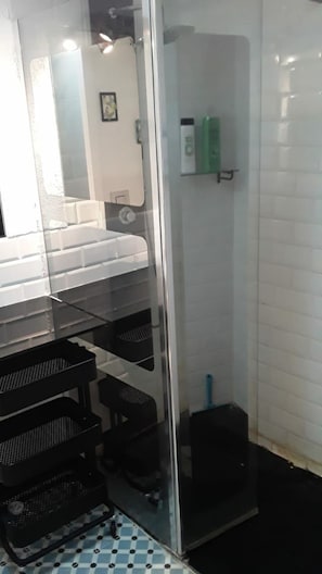 Un baño con cabina de ducha de vidrio, un lavamanos y un estante con artículos de aseo.