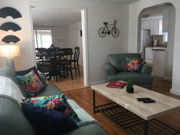 A living room with a sofa, a coffee table, and a dining area in the background.