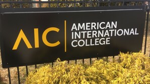 A sign for American International College with a black background and yellow lettering.