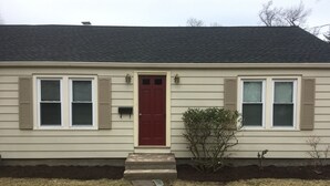 A single-story house with a red front door, beige siding, and a small garden area with stepping stones leading to the entrance.