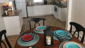 A kitchen with white cabinets, a refrigerator, a stove, and a sink. There is a dining table with blue and red plates and a lantern.