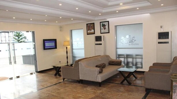 A lobby with a beige sofa, a small table, and a TV mounted on the wall. - De Brass Suites Hotel (Yenagoa)
