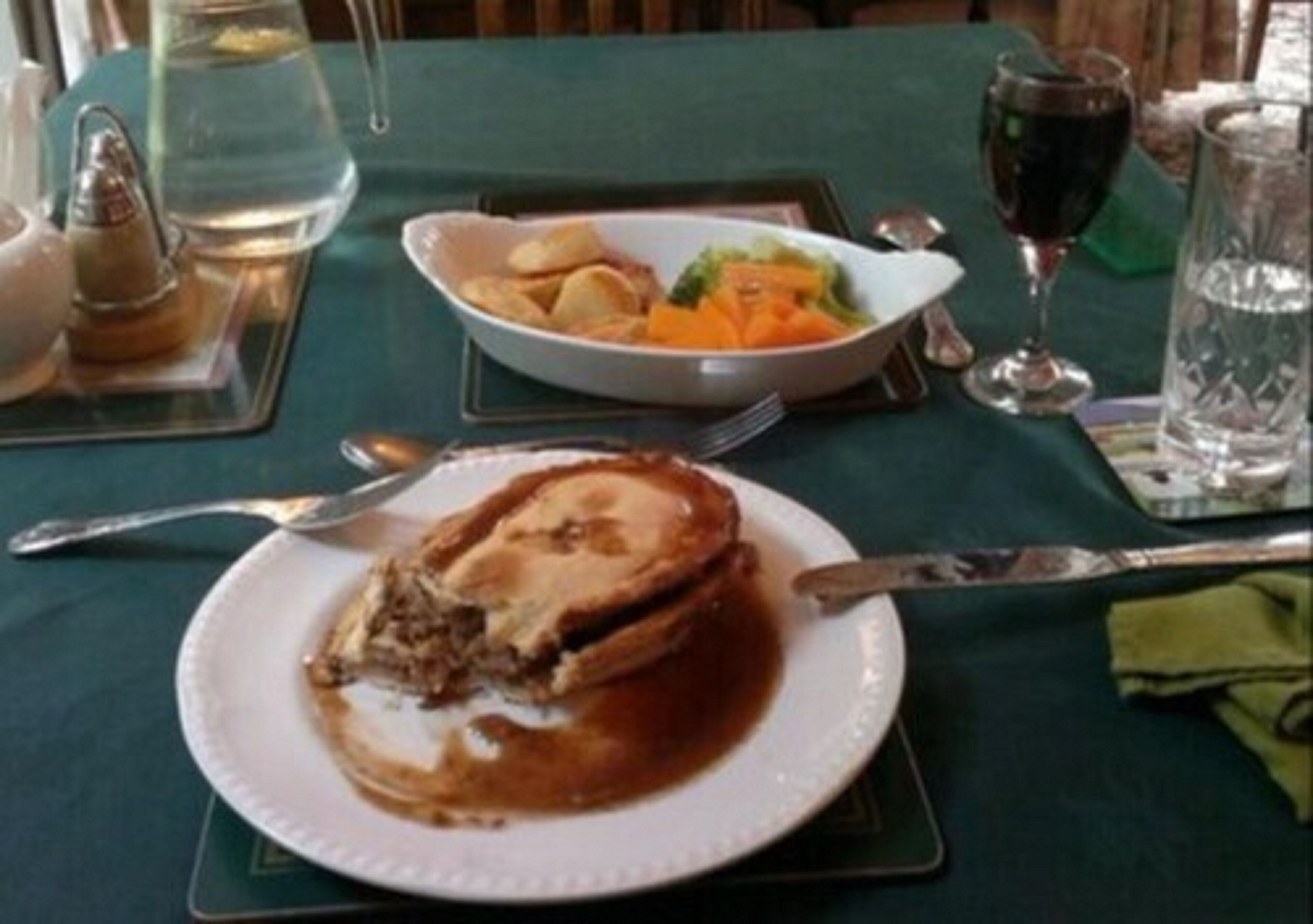 A dining table with a plate of food, a glass of red wine, and a pitcher of water.