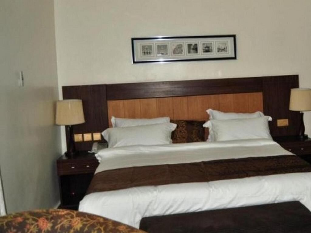 A hotel room with a large bed, two bedside tables, and a framed picture on the wall.