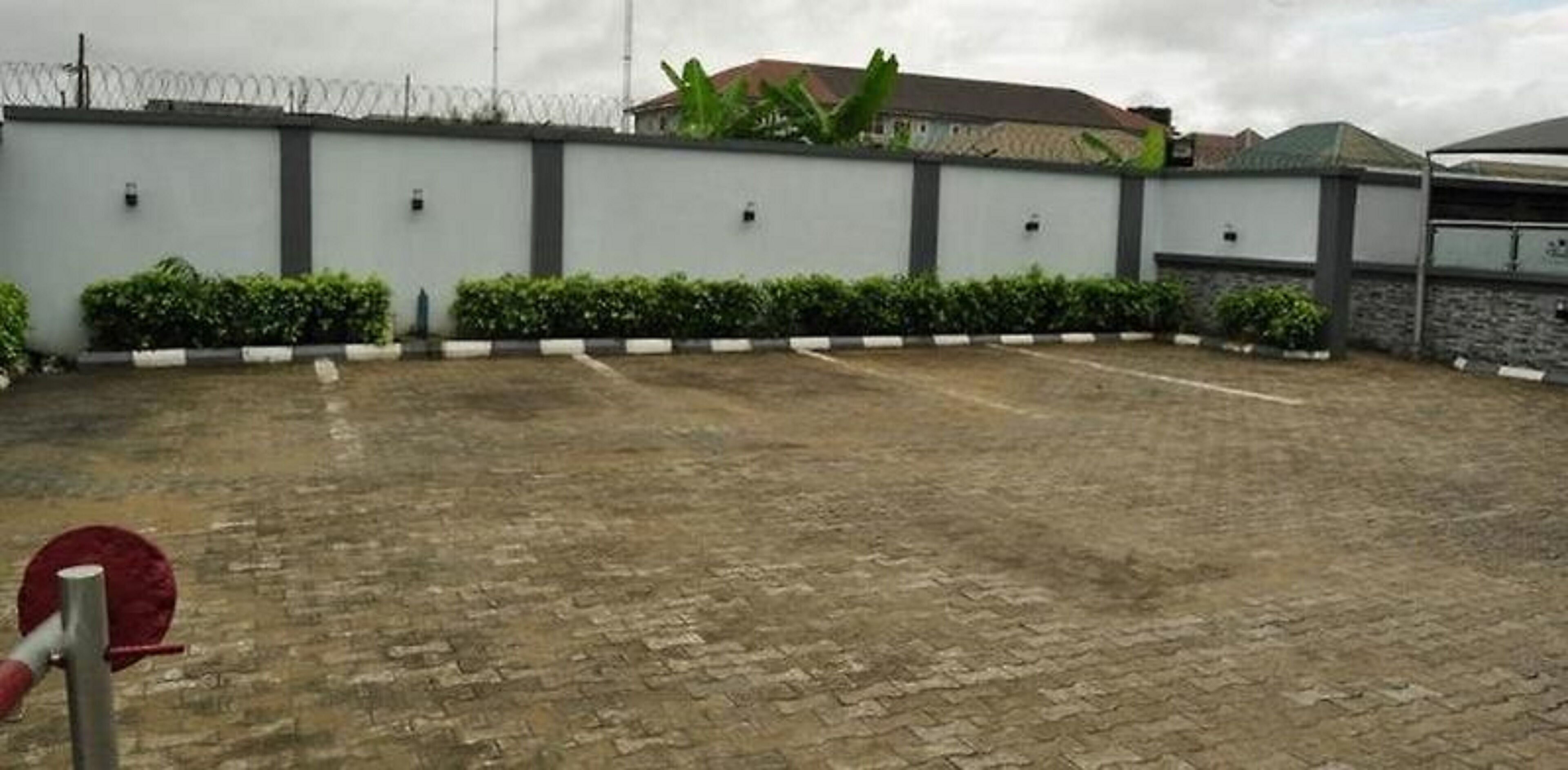 A paved courtyard with a low wall, a barbed wire fence, and a building with a sloped roof in the background.