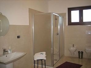 Un baño con ducha de vidrio, lavamanos, inodoro y un pequeño taburete con toalla.