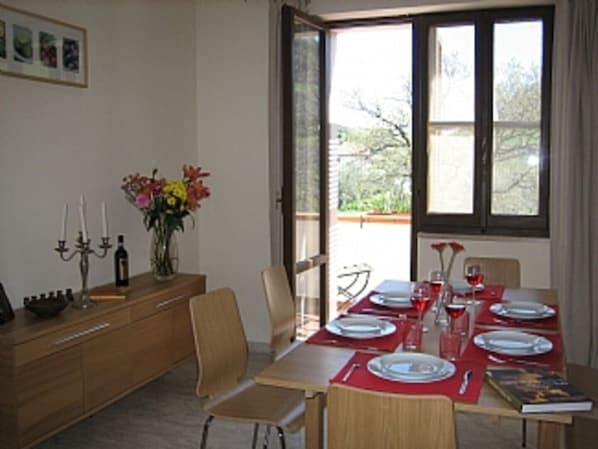 Un comedor con una mesa dispuesta para cuatro, un florero con flores y vistas al exterior a través de una ventana.