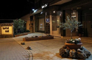 Entrada de hotel con un letrero, un pequeño jardín y una zona pavimentada.