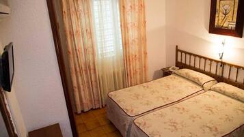 Quarto com duas camas, cabeceira de madeira, mesa de cabeceira, telefone fixado na parede e janela com cortinas.