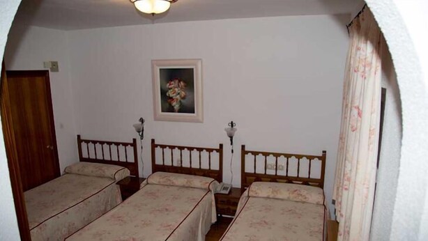 Une chambre avec deux lits simples, une tête de lit en bois, une petite table de chevet avec une lampe, un tableau encadré au mur et une porte.