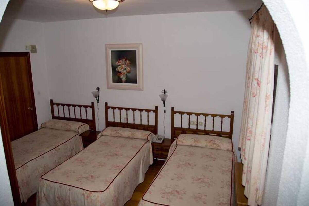 Een kamer met twee eenpersoonsbedden, een houten hoofdbord, een klein nachtkastje met een lamp, een lijst met een afbeelding aan de muur, en een deur.