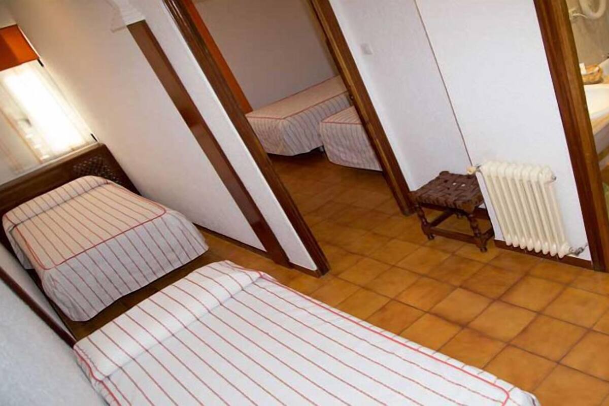 Een kleine, compacte kamer met twee bedden, een radiator en een klein krukje.
