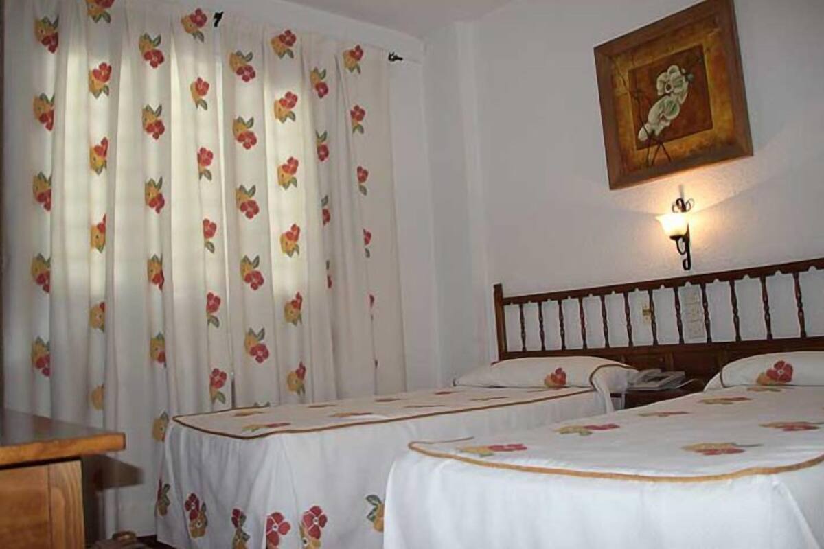 Een hotelkamer met twee bedden, bloemeninrichting, een houten hoofdeinde, een wandlamp en een lijst met een afbeelding.