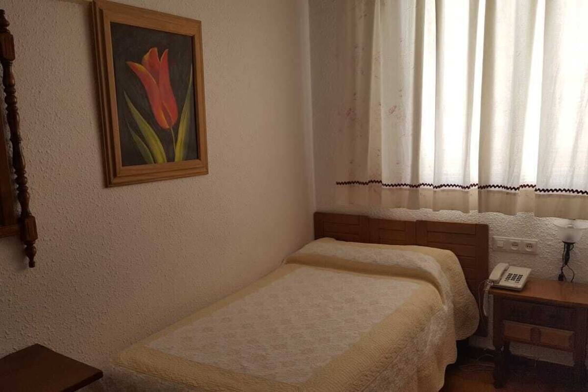 Een slaapkamer met een bed, een nachtkastje met een telefoon, een spiegel en een schilderij aan de muur.