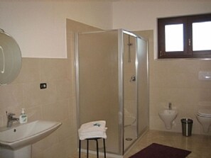 Une salle de bain avec une douche à parois de verre, un lavabo, des toilettes et un petit tabouret sur lequel est posée une serviette.