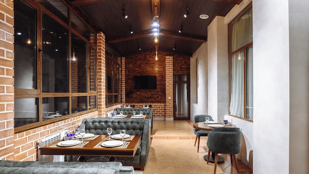 Un restaurant aux murs de briques, aux grandes fenêtres et au plafond haut avec des poutres apparentes. Les tables sont dressées avec des assiettes et des verres.