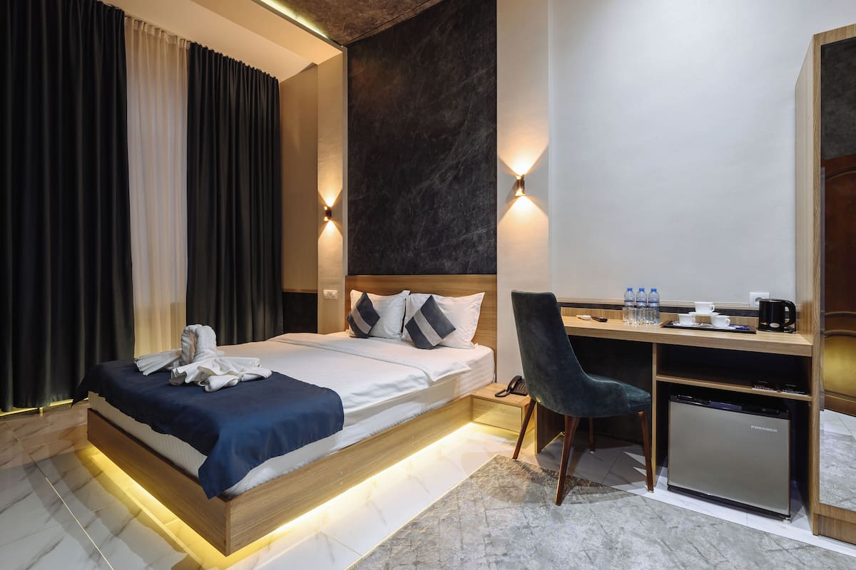 Une chambre d’hôtel moderne équipée d’un lit, d’un bureau, d’une chaise et d’un petit réfrigérateur.