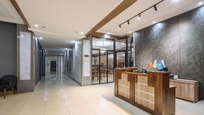 Un hall d’hôtel moderne comprenant un comptoir d’accueil, un espace salon et une cloison en verre donnant sur une salle à manger.