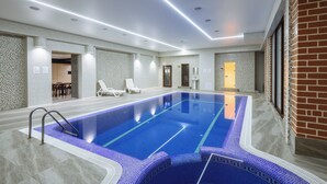 Une grande piscine intérieure à l’eau d’un bleu limpide, entourée d’un mur recouvert de carreaux et d’une partie en briques.