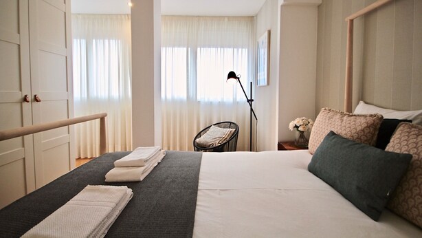Habitación de hotel con cama, una silla, una lámpara y una ventana con cortinas.