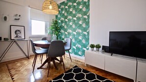Un comedor moderno con una mesa redonda, sillas, una lámpara colgante y un papel tapiz con motivos tropicales.