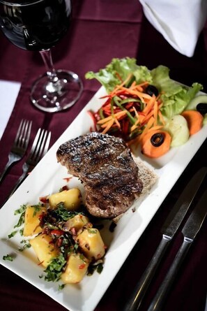 A steak, a salad, and a glass of red wine on a table.