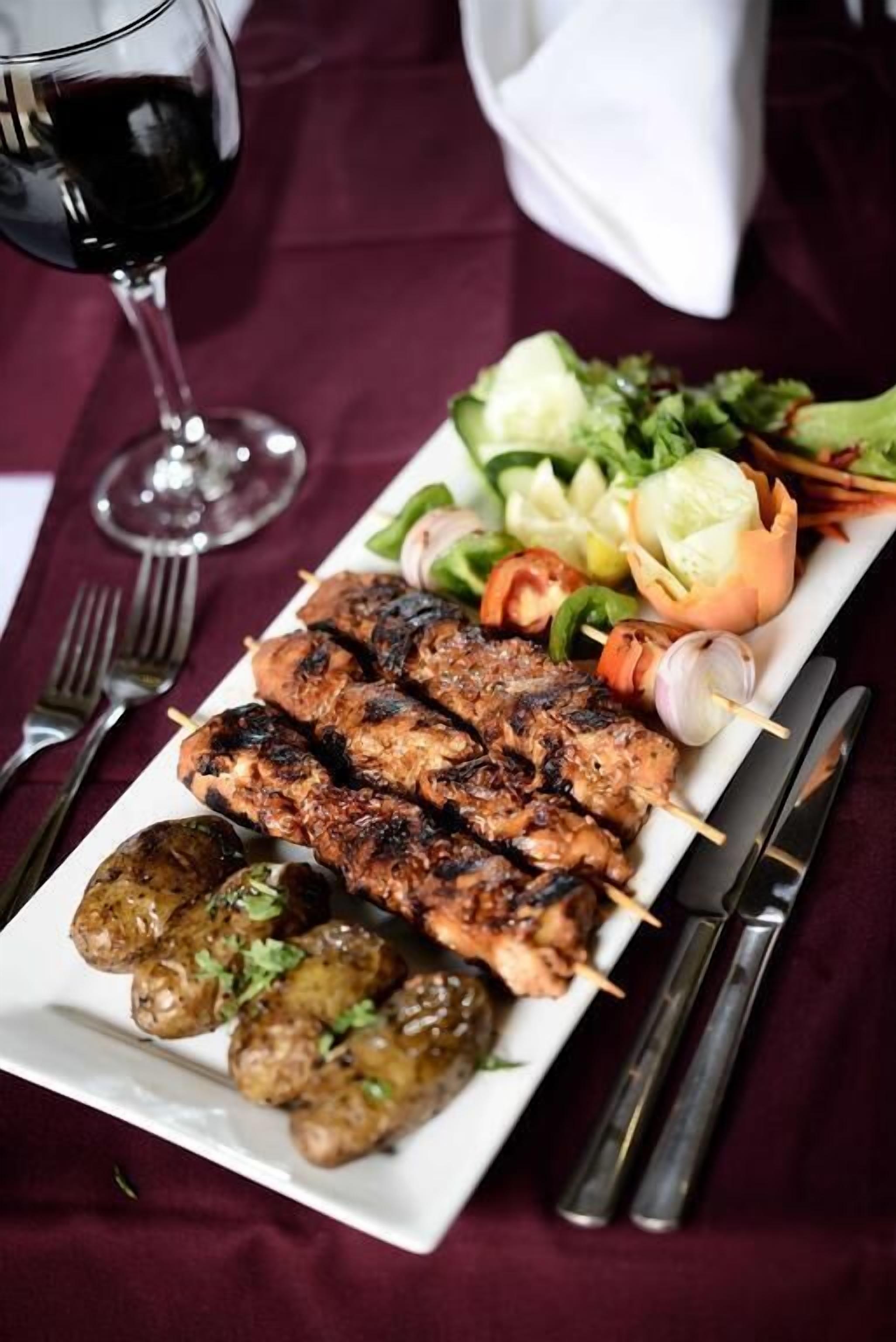 Un plato de brochetas de carne a la parrilla, ensalada y verduras asadas sobre un plato blanco.