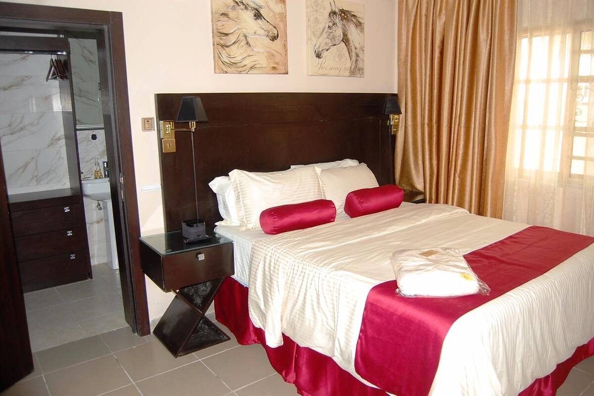 A hotel room with a large bed, a wooden headboard, a nightstand, a mirror, and artwork on the wall.