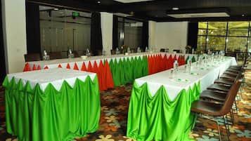 Un salón de conferencias con mesas largas, cortinas verdes y rojas, y una alfombra estampada.