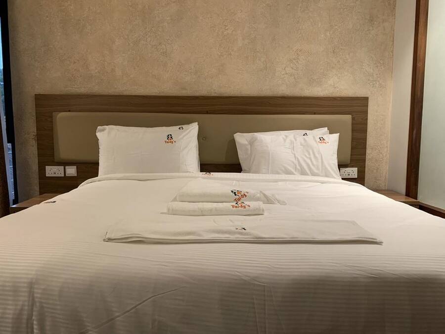 Una cama bien hecha con sábanas y almohadas blancas, un cabecero de madera y una mesita de noche con una lámpara.