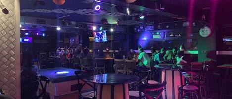 A bar with tables and chairs, a stage with performers, and a DJ booth.