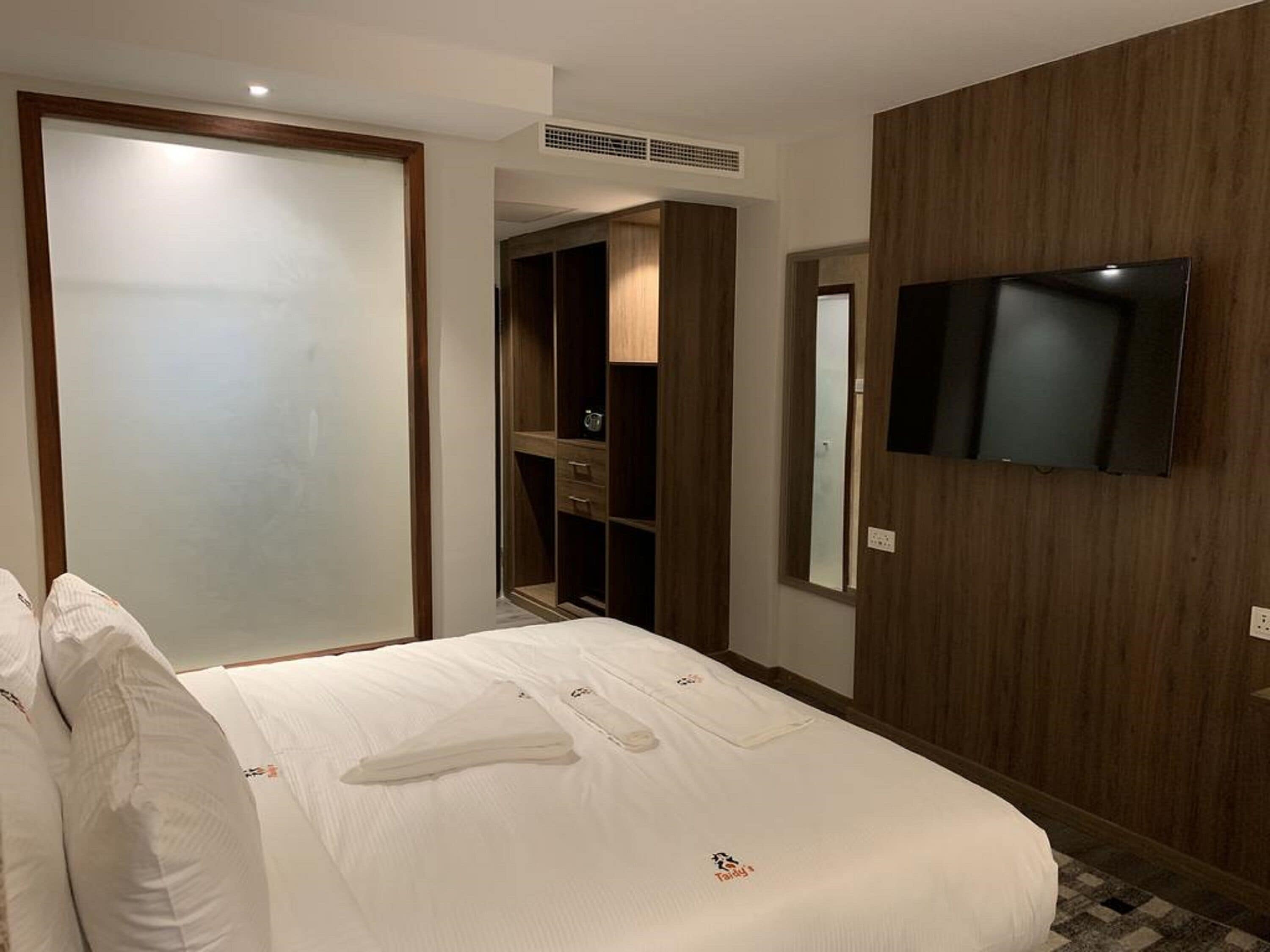 Habitación de hotel con cama, televisor montado en la pared, armario y ropero.
