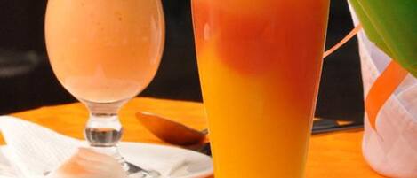 Dos vasos de jugo de naranja sobre una mesa, con una servilleta, cuchara y tenedor.